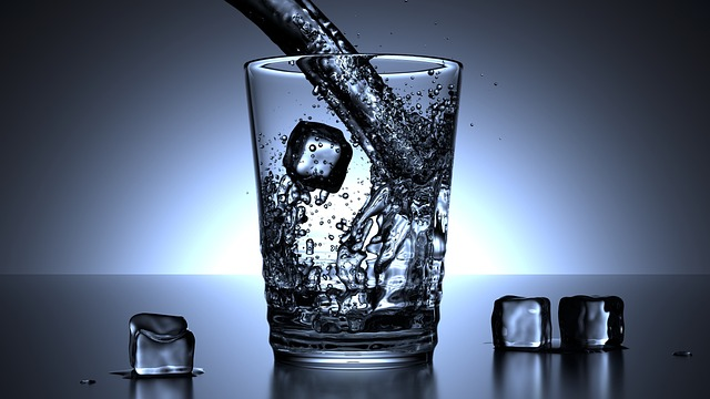 An image of water being poured into a glass with ice cubes. 