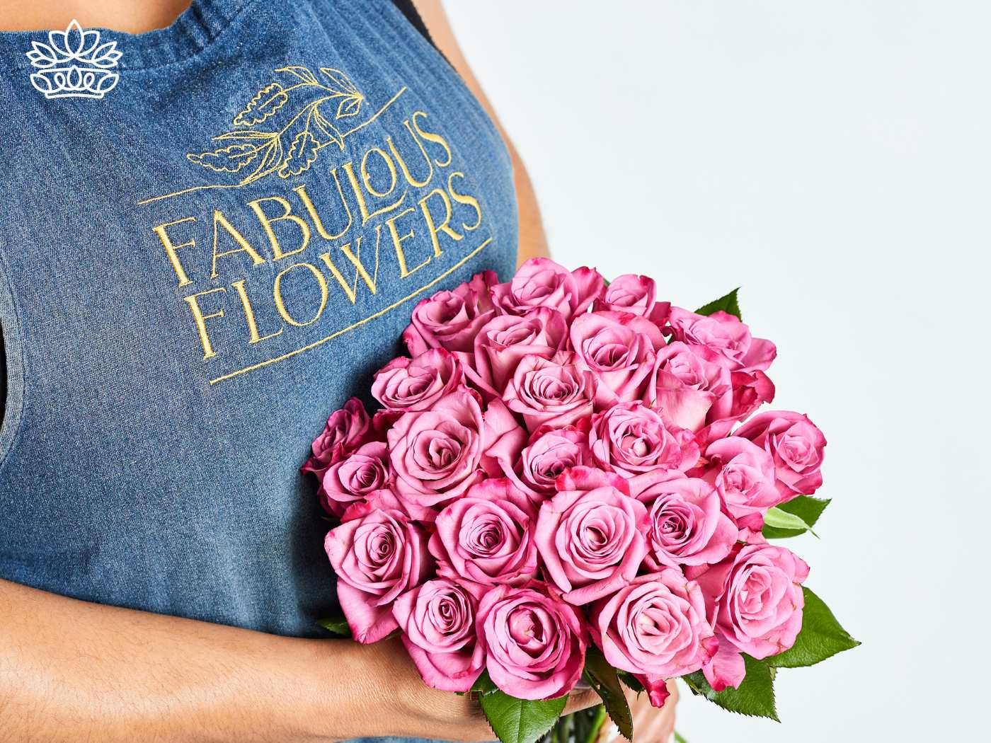 A florist wearing a denim apron embroidered with 'Fabulous Flowers' cradles a bouquet of vibrant pink roses, symbolizing creativity, beauty, and a thoughtful gift idea. Fabulous Flowers and Gifts. Gifts for Her.