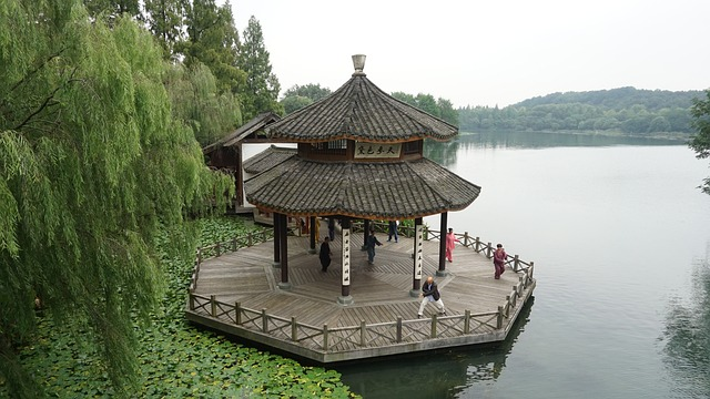 Image by James_Peng from Pixabay. Gazebo on the edge of a lake with a group of people practicing Qigong. 