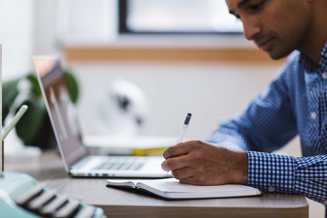 Man doing research on laptop and writing in notebook