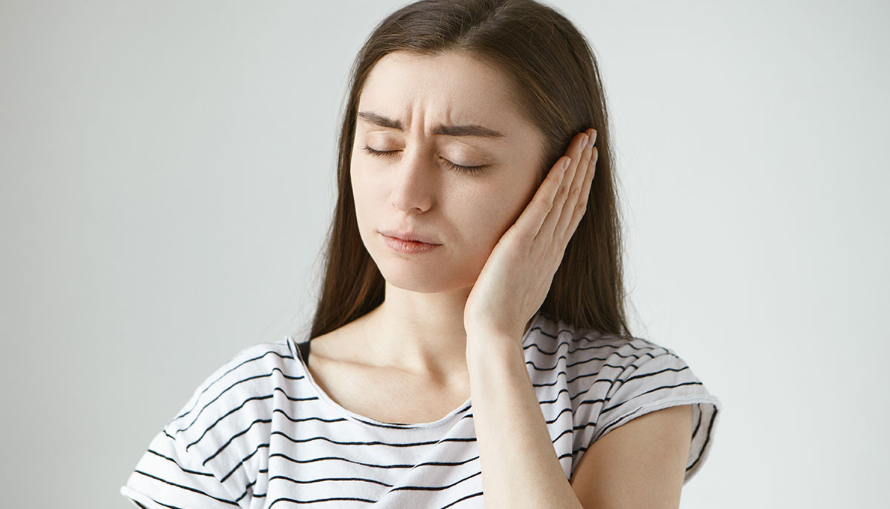 Kvinne med smerte uttrykk holder seg for øret.