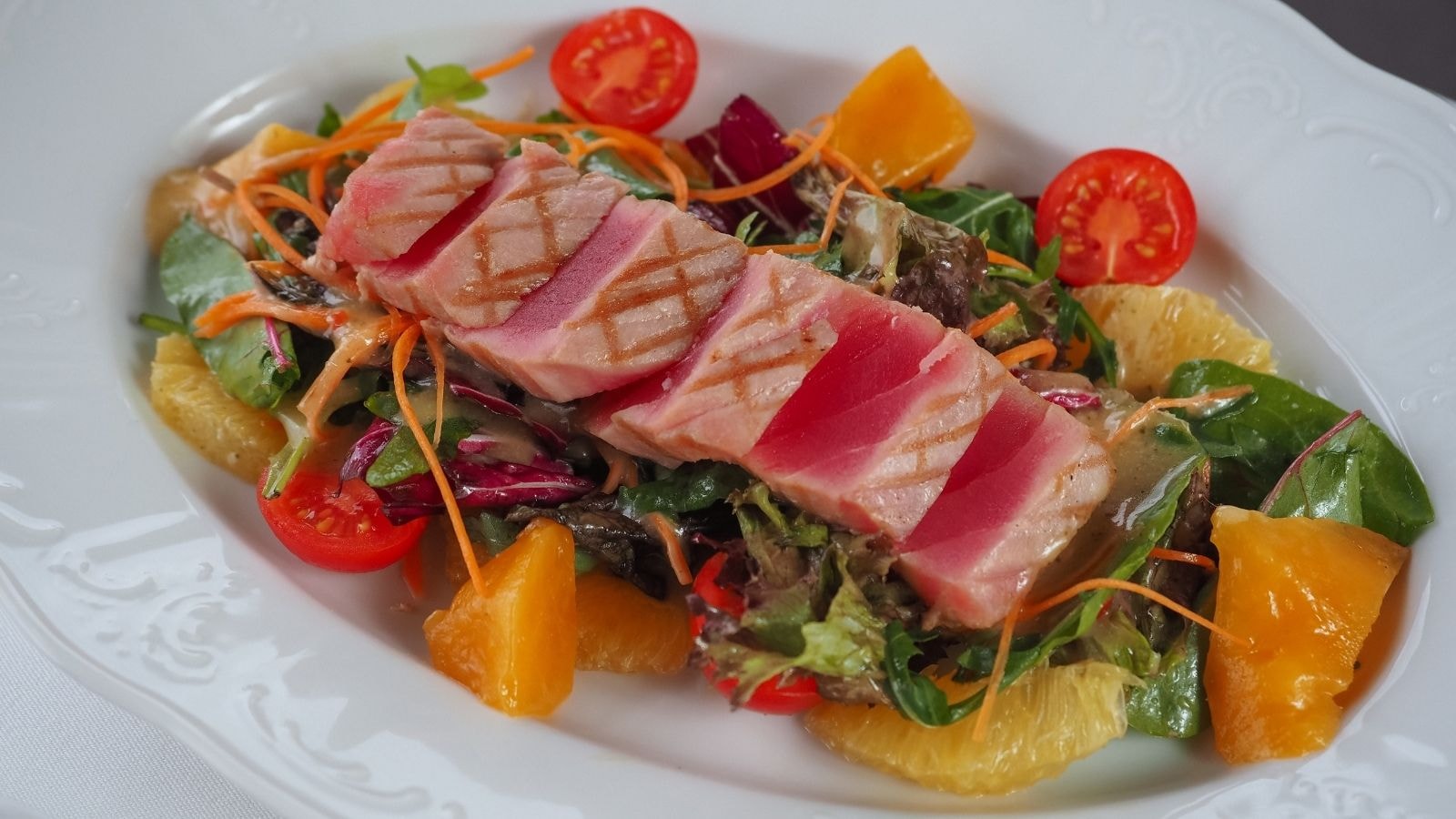 Seared tuna slices on mixed vegetable salad with tomatoes and oranges