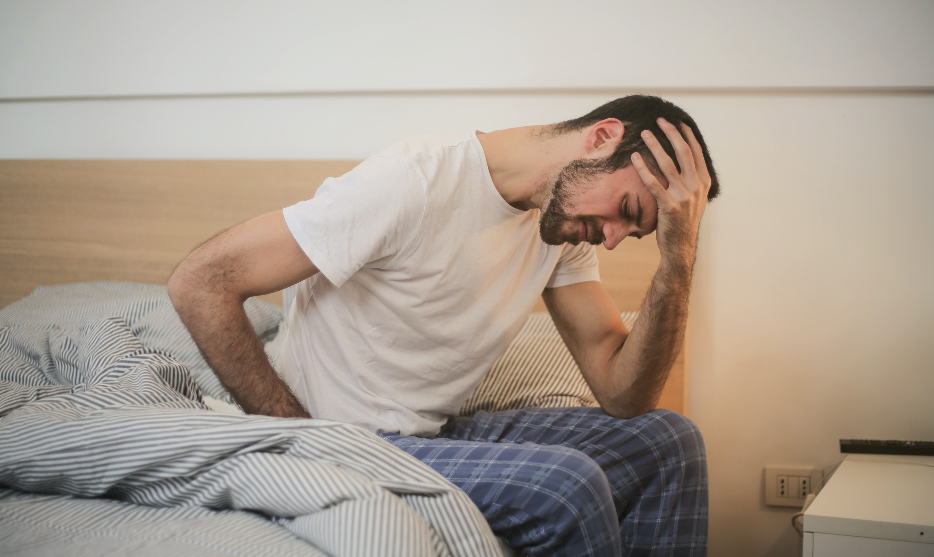 a man sits with his head in his hands on a bed to represent the question: what are the side effects of hydrocodone?