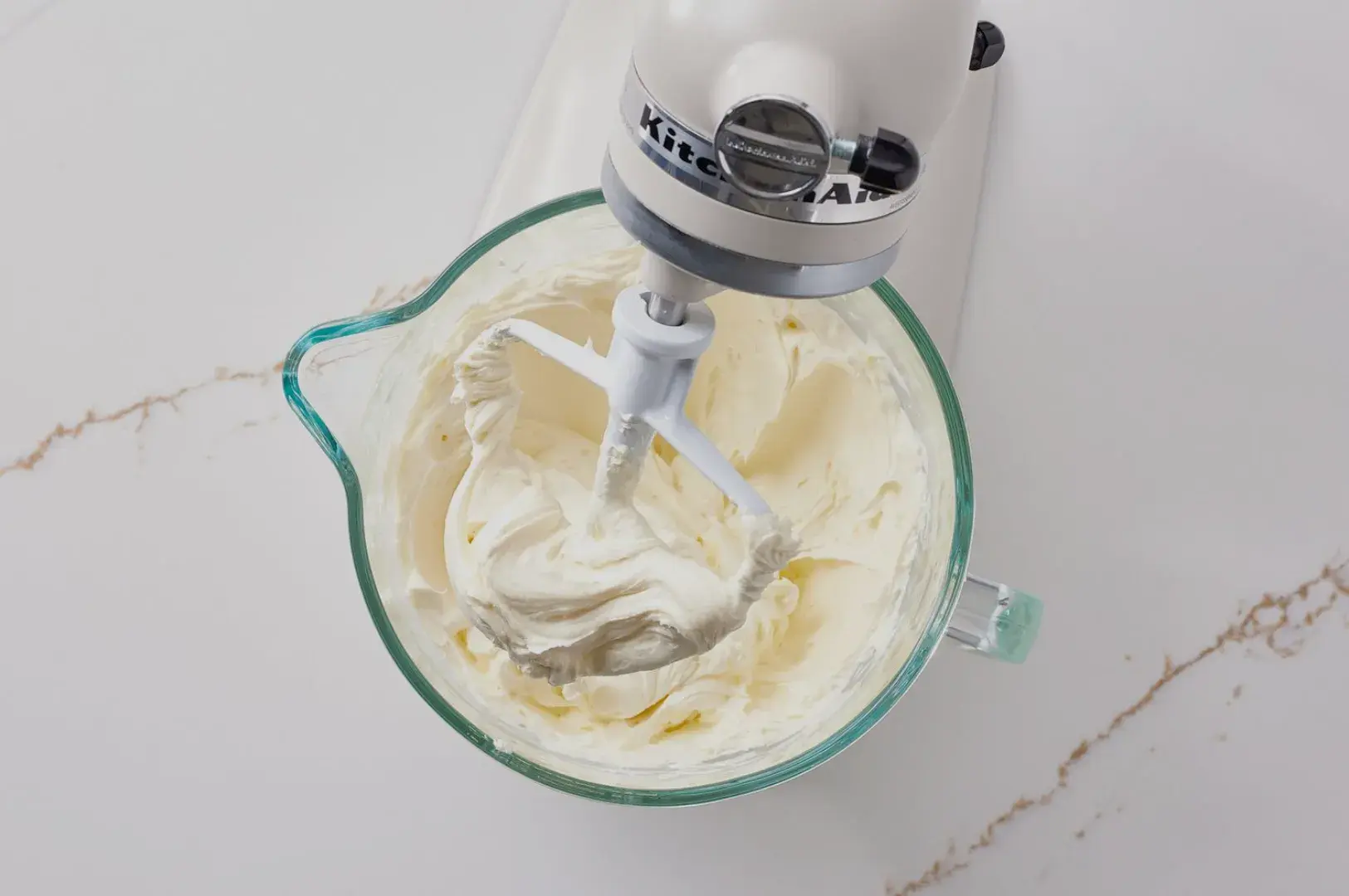 A mixing bowl with a stand mixer, containing whipped cream or frosting.