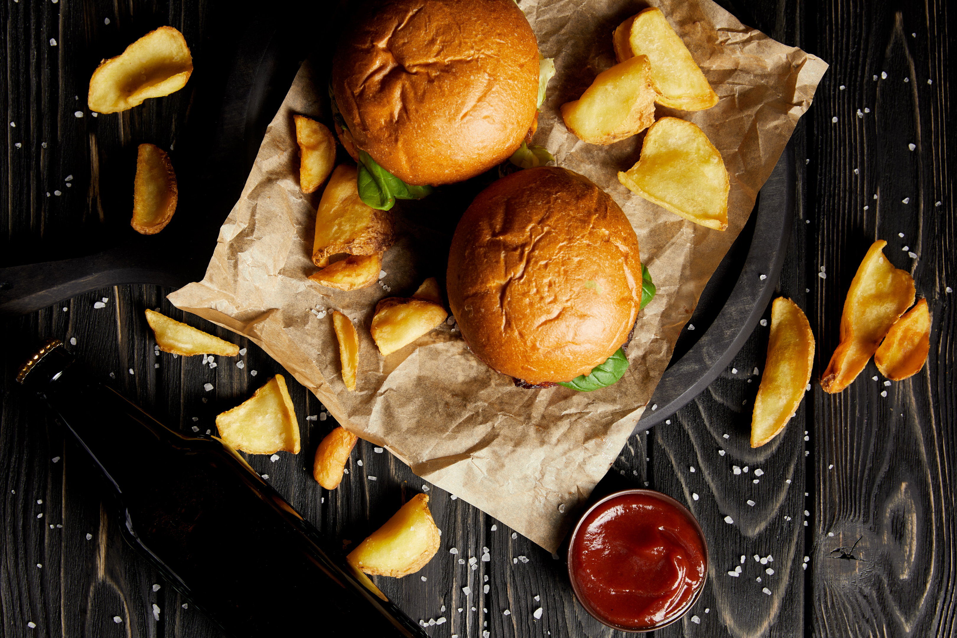 burgers on a wooden board and craft paper with a beer bottle next to them