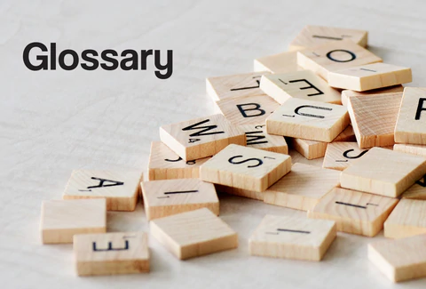 A mix of Scrabble letters randomly scattered on a table top. The word – Glossary – can be seen