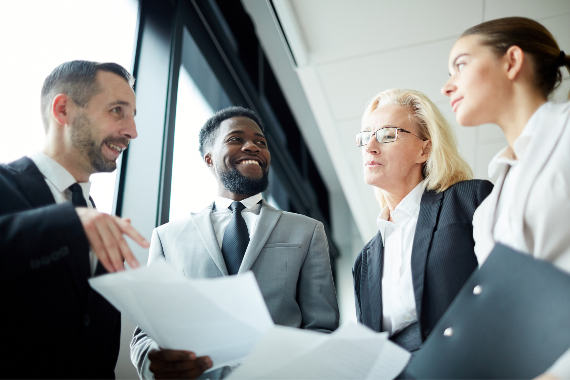 Group of business brokers in formal attire discussing documents during a team meeting