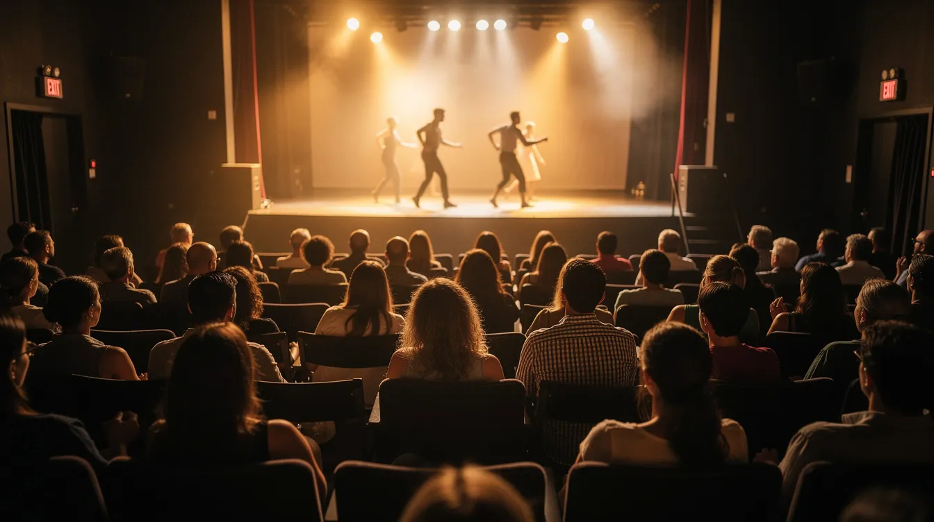The image shows an audience attentively watching a dance performance in a cozy community theatre, illuminated by warm stage lighting that enhances the intimate atmosphere of the event. The scene captures the engagement of the audience, highlighting the importance of participation in community events.