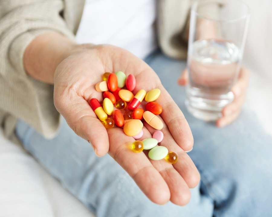 Close-up of colourful nutritional supplements in hand with a glass of water – Supplements Nutrition from The Good Stuff