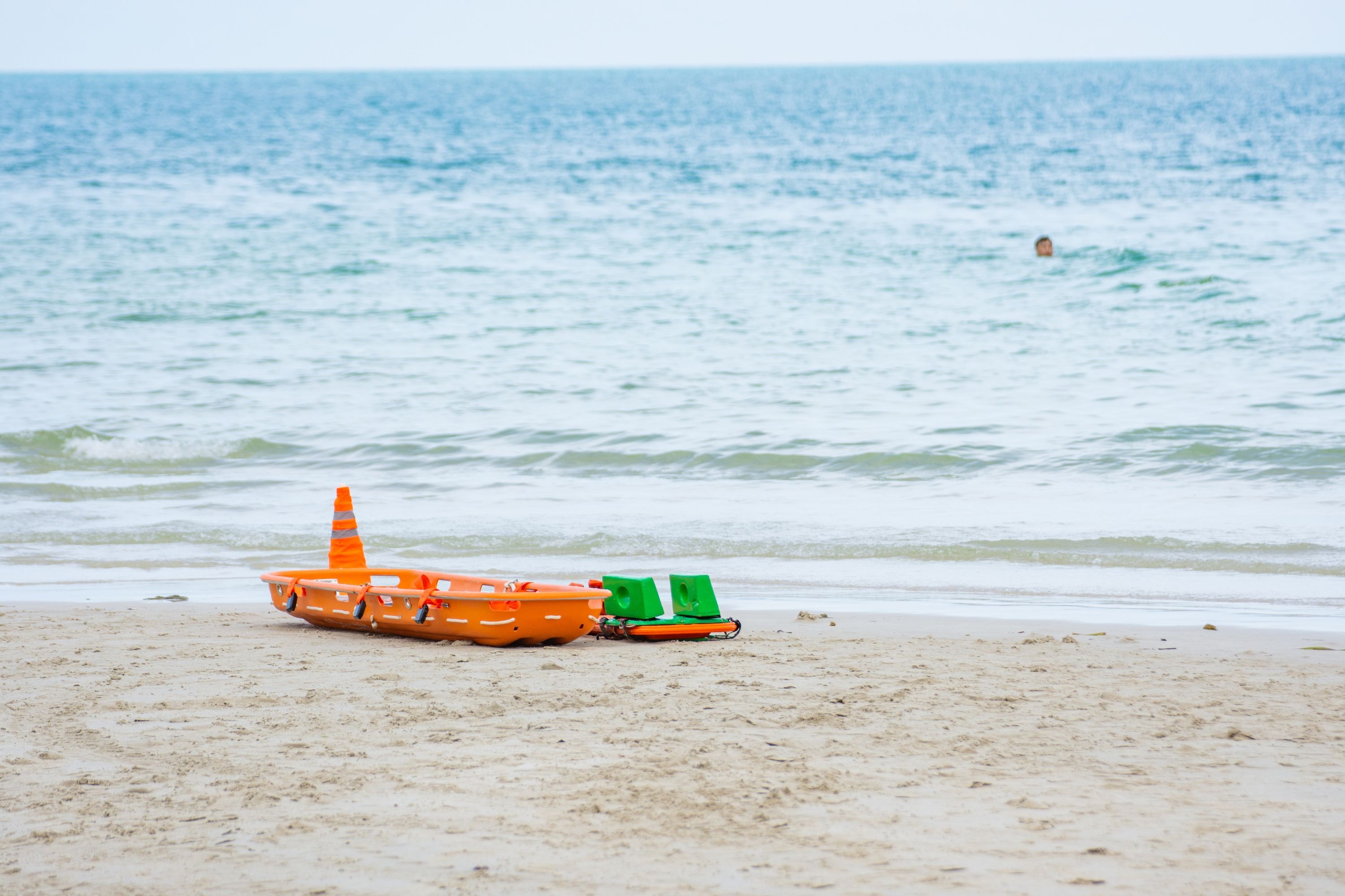 Orange spine board with head immobilizers placed on a beach, showcasing lightweight backboard design.