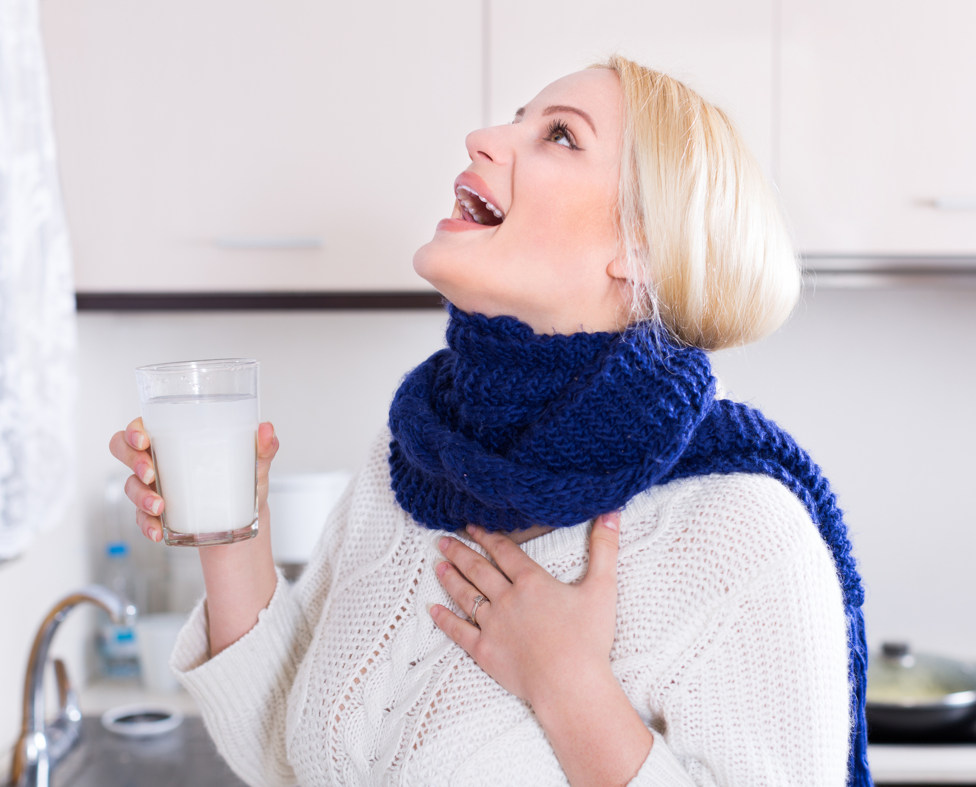 An image of a woman gargling with warm salt water at the kitchen sink. 