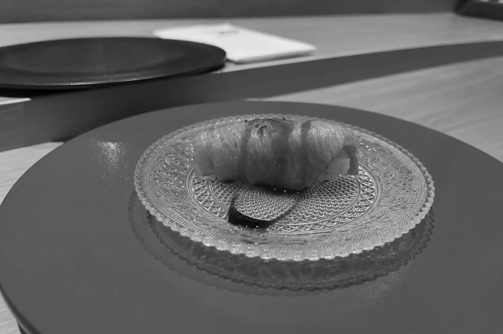 Seared sushi roll presented on a decorative glass plate with a touch of sauce.