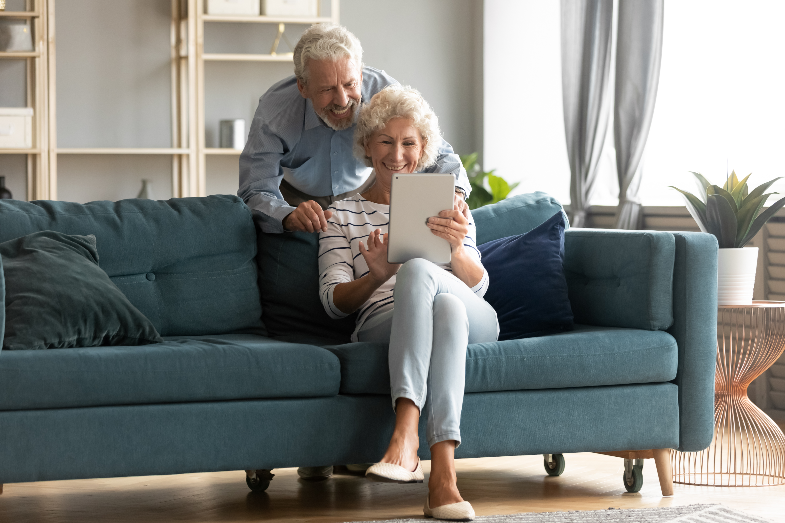 an elderly couple watch something funny on a tablet in their living room