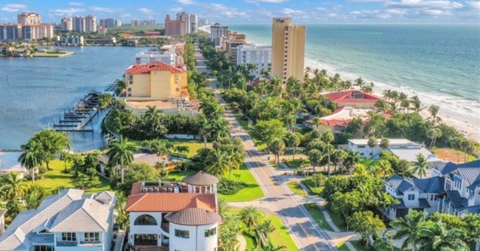 The image features a vibrant resort-style pool area surrounded by lush palm trees, with well-maintained tennis courts nearby, creating an idyllic setting for relaxation and recreation in the Vanderbilt Beach neighborhood of Naples, FL. This picturesque scene embodies the luxurious lifestyle associated with Vanderbilt Beach real estate, offering residents ample opportunities for outdoor activities and leisure.