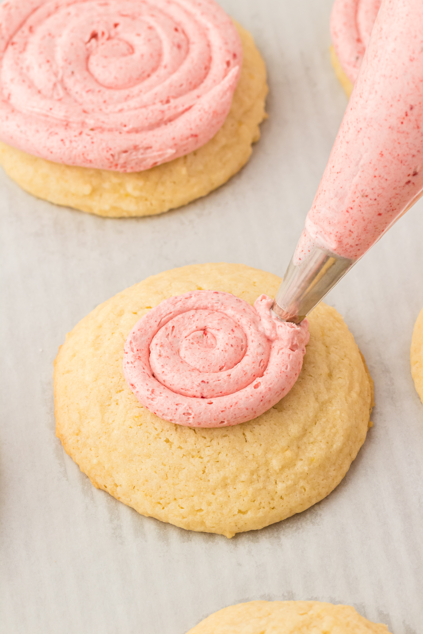 piping bag piping strawberry frosting in a circle pattern onto a lemon cookie