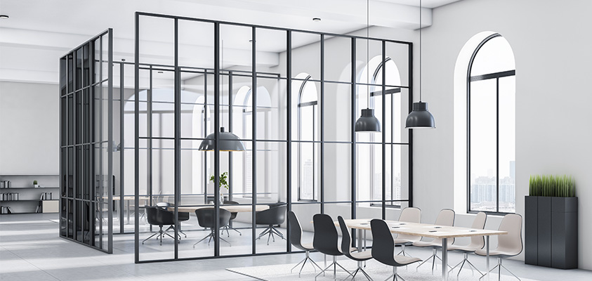 A large black and white office space. Glass and metal floor to ceiling room dividers have been installed to create a small meeting space in the middle of the room.