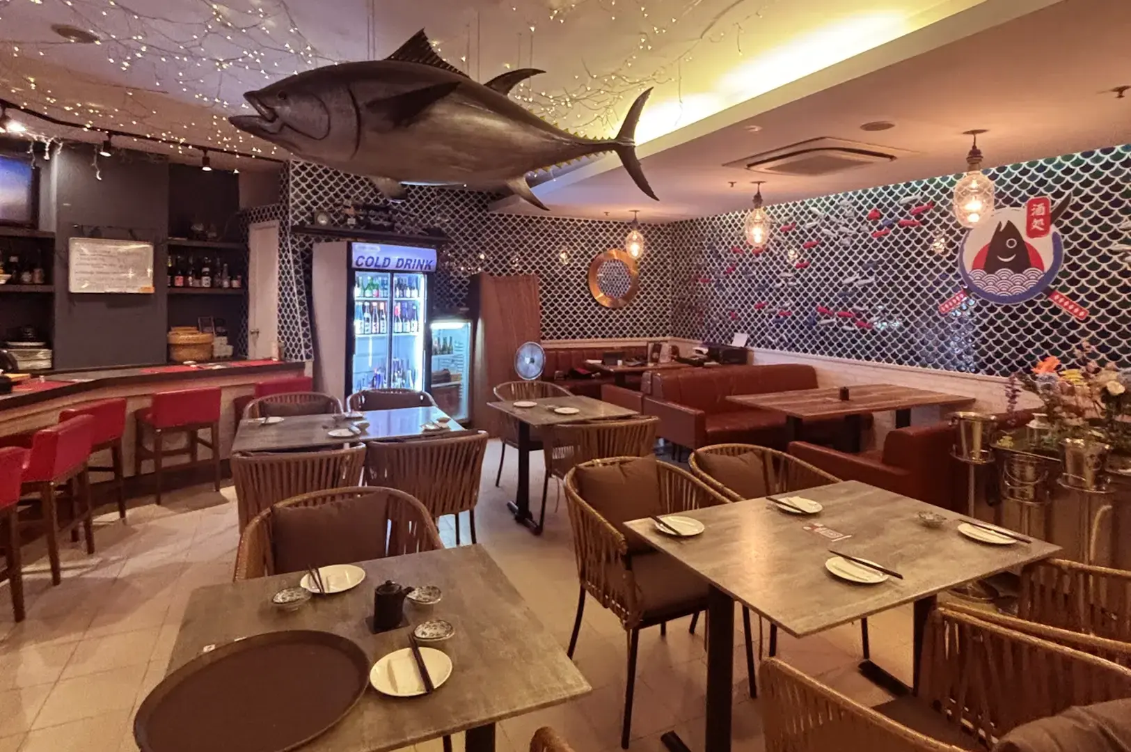 Maguro Samurai dining room with set tables, red and brown seating, fish-scale patterned walls, hanging lights, and a large tuna sculpture suspended from the ceiling.