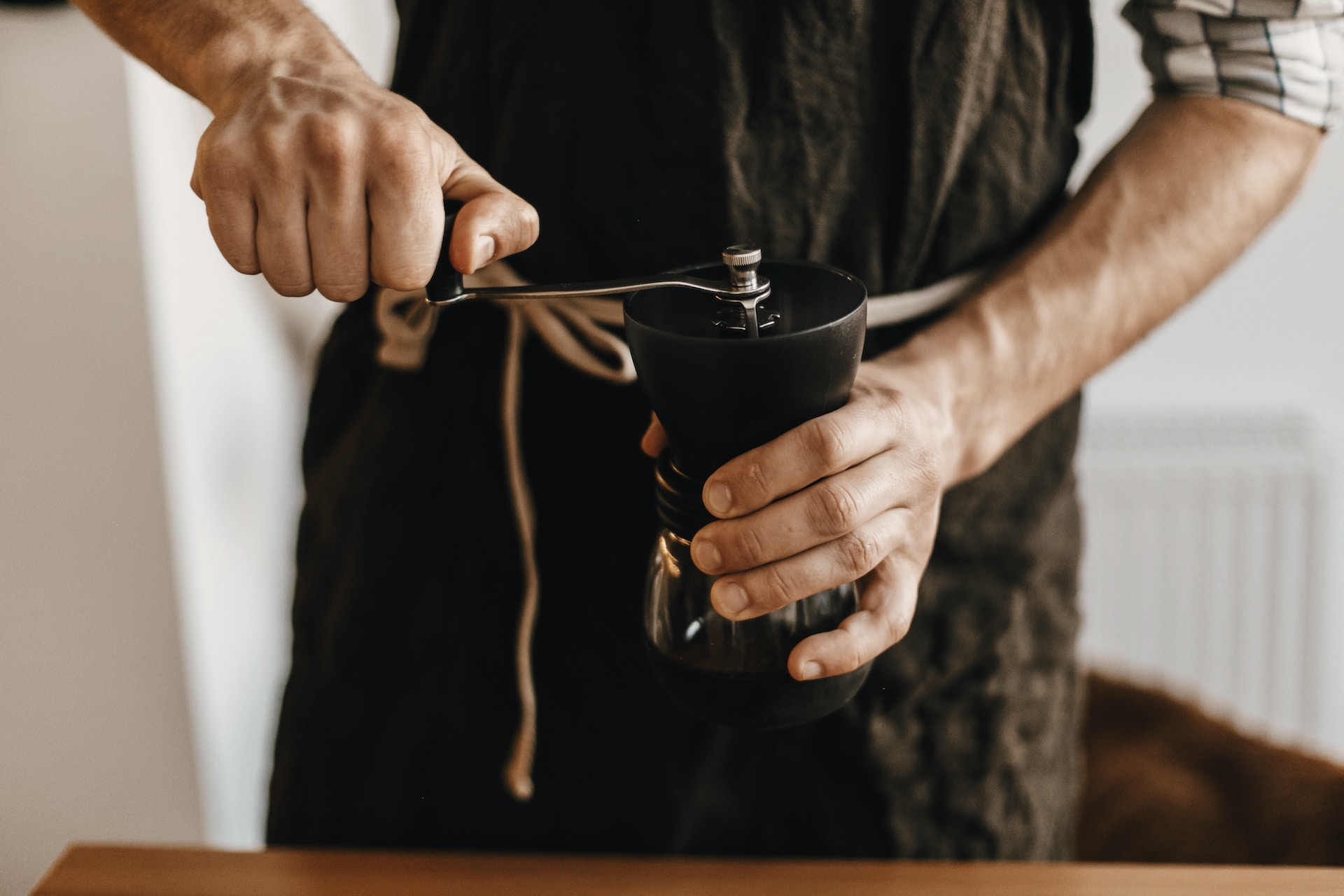 A man twists the top of a black manual coffee grinder