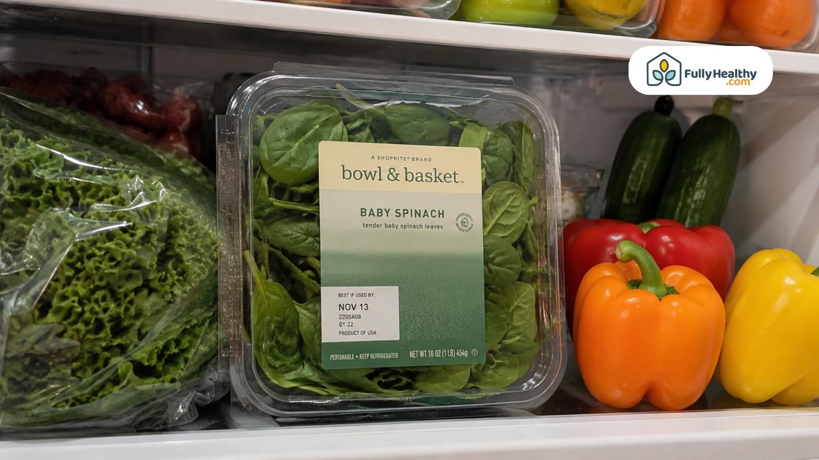 Baby spinach clamshell stored neatly on refrigerator shelf with vegetables