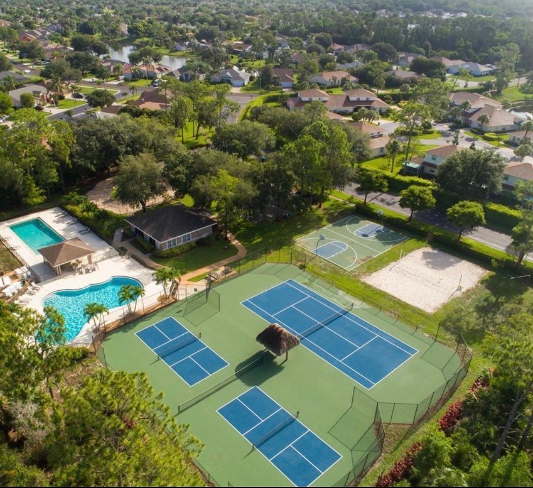 The image depicts an elegant entrance to a gated community, featuring tall palm trees and a security gatehouse that welcomes residents and visitors. This desirable gated community in Naples, FL, offers convenient access to amenities such as community pools and recreational facilities.