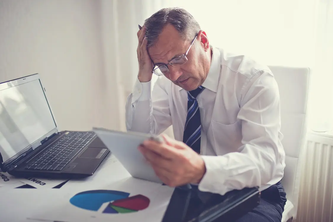 Business owner reviewing messy financial documents while inattentive broker shows signs of rushed or lazy pricing strategy.