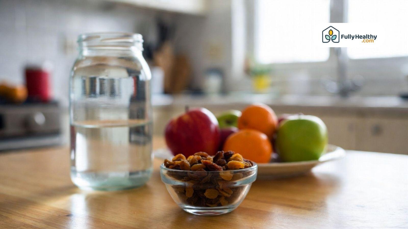 Glass bowl of raisins beside water and fresh fruit on a kitchen table for constipation support.
