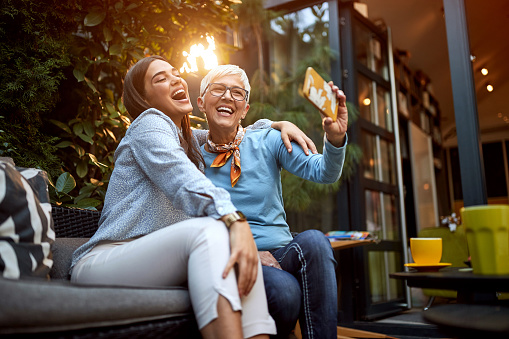 Two happy mature women sitting outside at night taking a selfie.