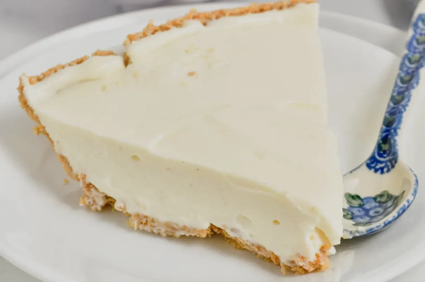 A slice of creamy cheesecake on a white plate with a decorative spoon beside it.