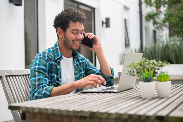 Cheerful young man sitting outside and working on a laptop.  