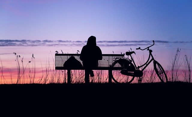someone sitting on a bench, looking at the sun set, pondering 