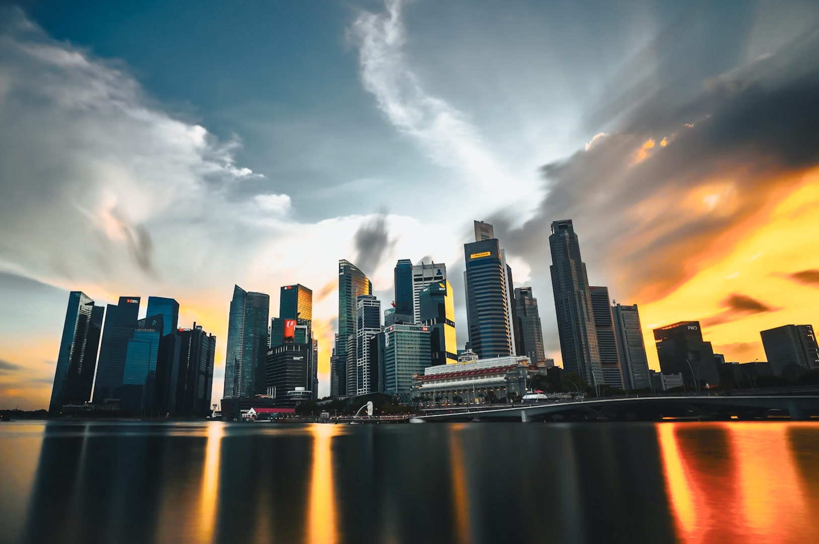 Panoramic Singapore city skyline with reflections on the water and dramatic clouds.