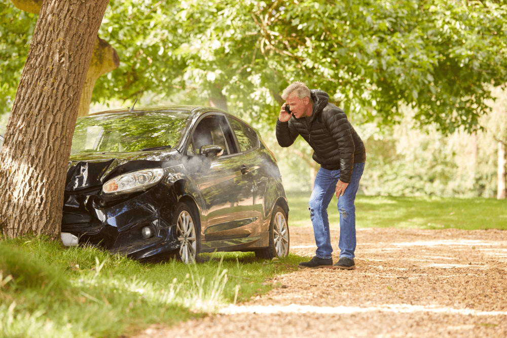 @Envato Elements | Wypadek - mężczyzna uderzył samochodem w drzewo i dzwoni po pomoc. Auto wymaga naprawy. Mężczyzna zgłasza szkodę. Pojazd w opłakanym stanie.