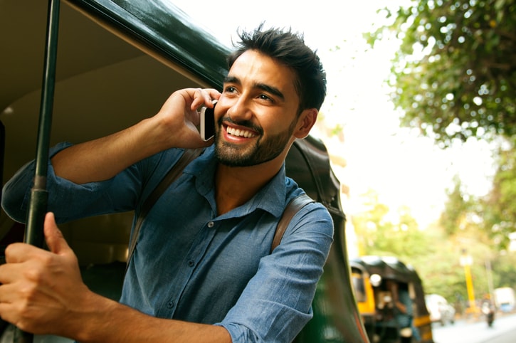 Young man in a blue shirt smiling and talking on a cell phone. 