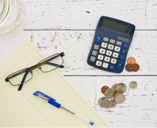 alt="An image with various tools of accounting: a pen, a balance sheet, a calculator, eyeglasses, and coins"
