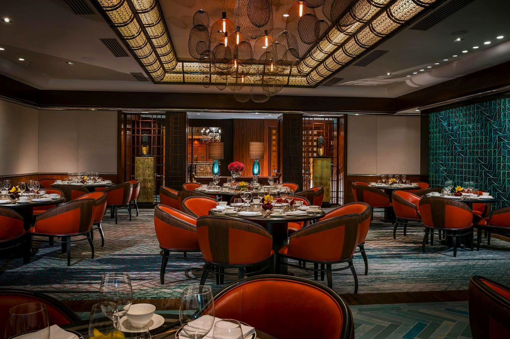 Luxurious restaurant interior with round tables and orange cushioned chairs, elegant lighting, and decorative vases. Warm ambiance and sophisticated feel.