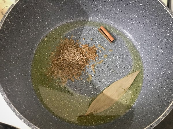 Bay leaf, cinnamon, and jeera (cumin seeds) simmering in oil in a pan.