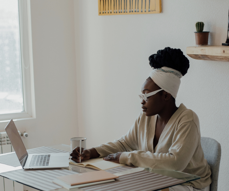 A woman sitting at her dining table while working on a laptop and writing