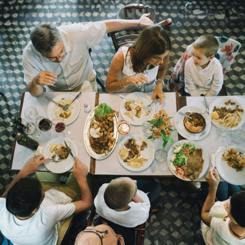 A senior Malaysian family is gathered around a dinner table, engaging in lively conversation and sharing laughter, highlighting the warmth of familial bonds. The scene captures the essence of human interaction, where the nuances of speech and hearing ability play a vital role in their connection.