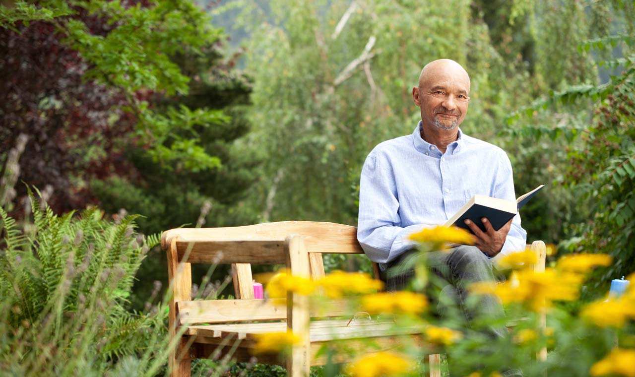 Mann sitzt auf DIY Gartenbank und erfreut sich über verschiedene Dinge und ein Buch.