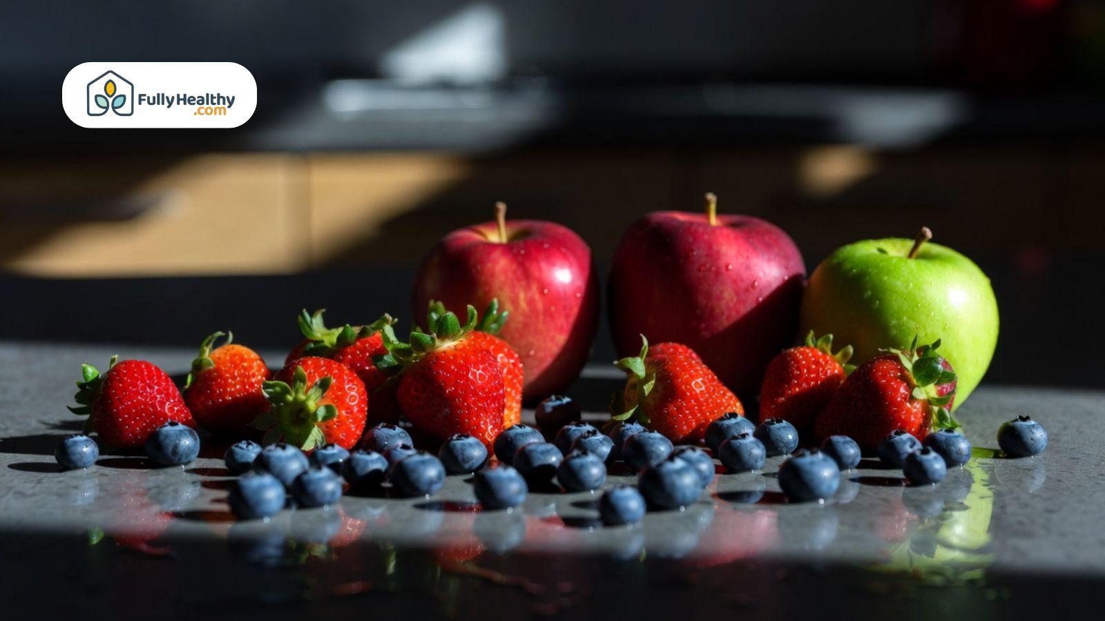 Fresh strawberries, blueberries, and apples arranged on a kitchen counter with dramatic natural sunlight.