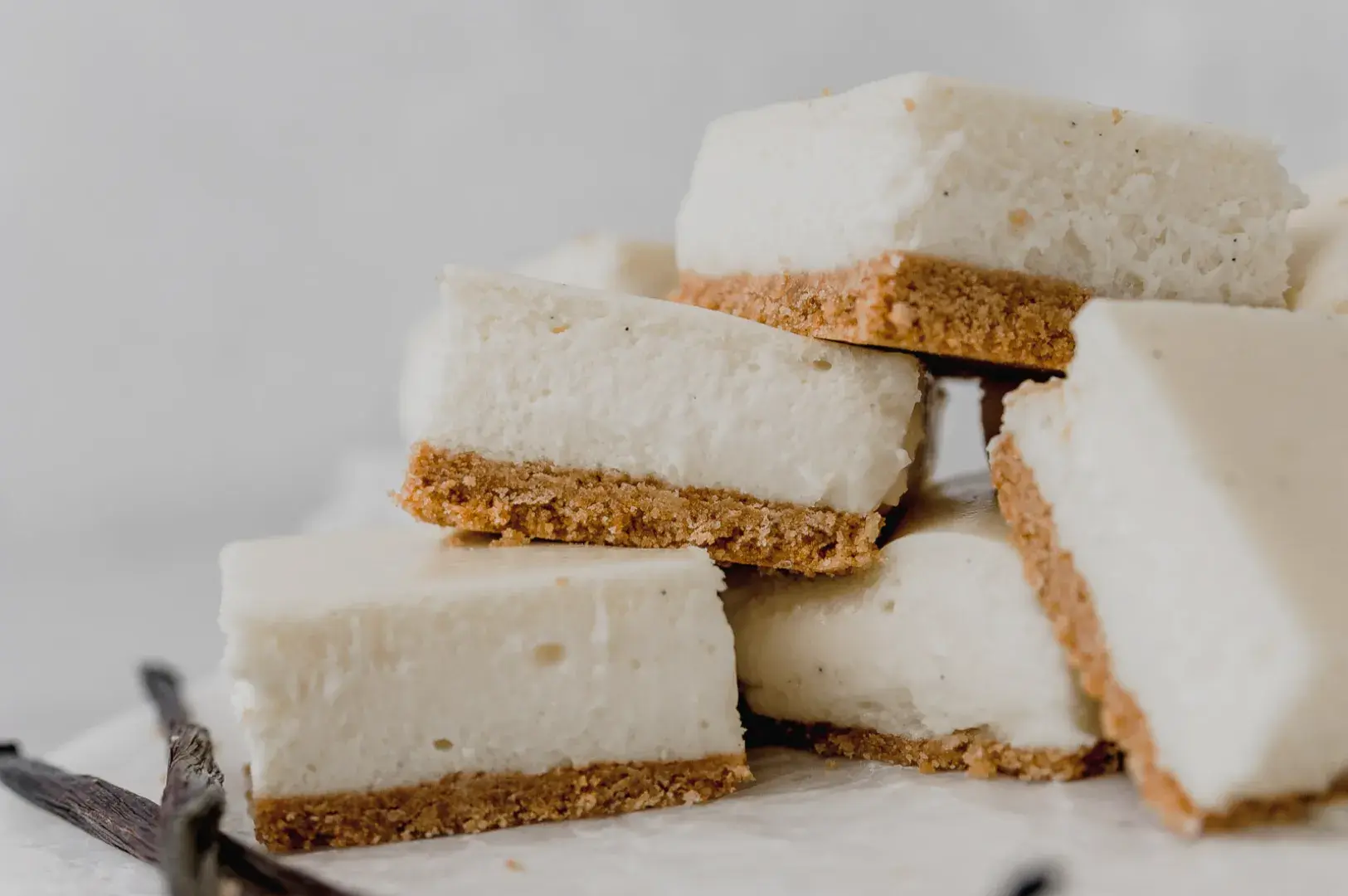 A stack of creamy cheesecake squares with a graham cracker crust, arranged on a light surface.