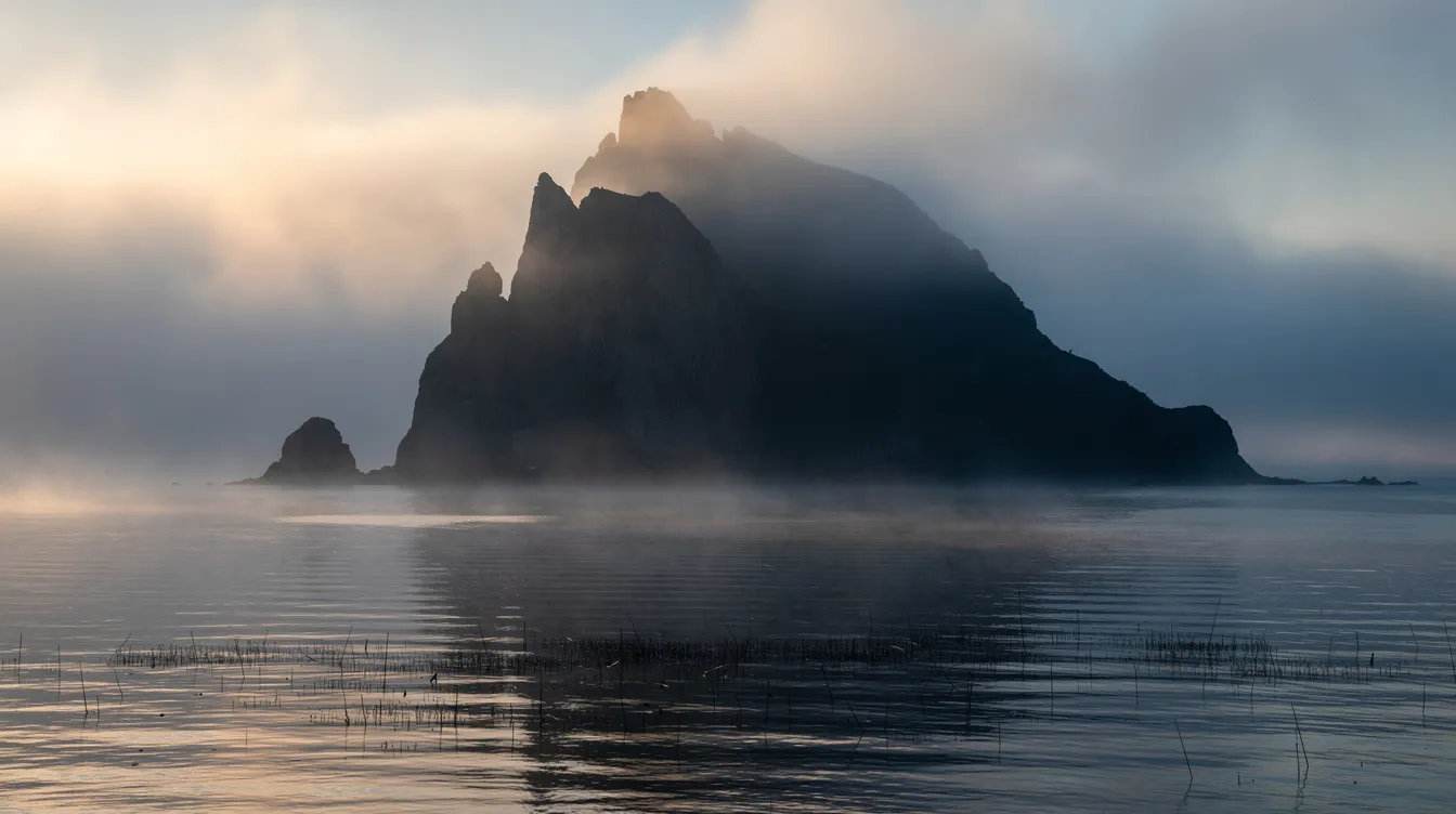 Die Silhouette einer nebelverhangenen Felseninsel erhebt sich majestätisch im sanften Licht des Tagesanbruchs, während das ruhige Meer im Vordergrund die geheimnisvolle Atmosphäre eines Psychothrillers wie „Shutter Island“ verstärkt. Die verschwommenen Konturen der Insel vermitteln ein Gefühl von Wahn und Realität, das an die spannenden Wendungen in Martin Scorseses Verfilmung erinnert.