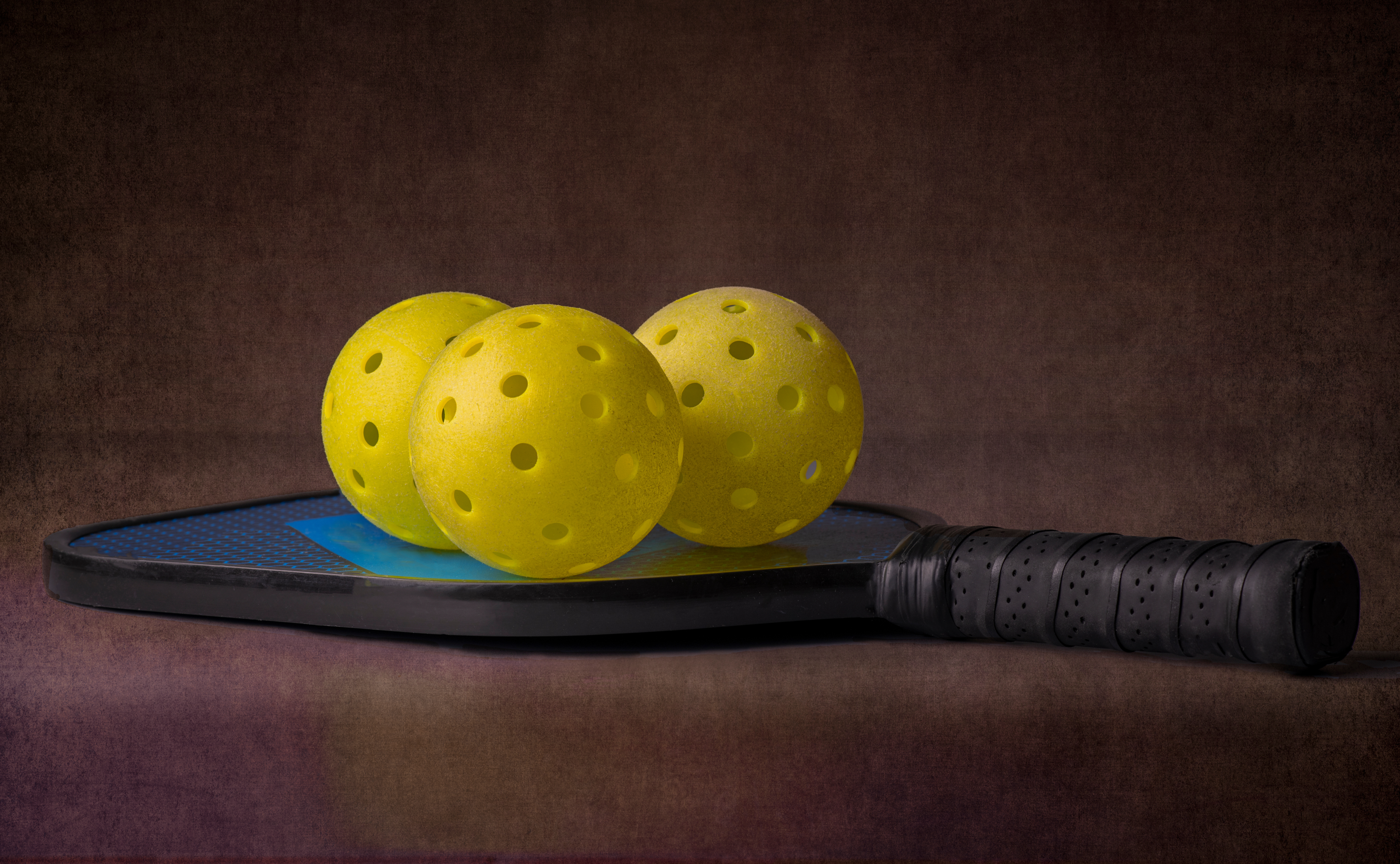Pickleball balls sitting on top of pickleball racquet