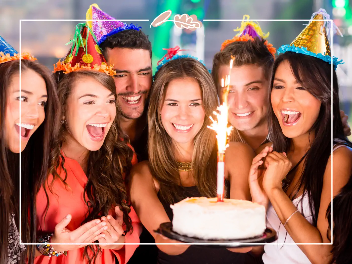 Group of friends celebrating a birthday with a cake and party hats, fabulous flowers and gifts