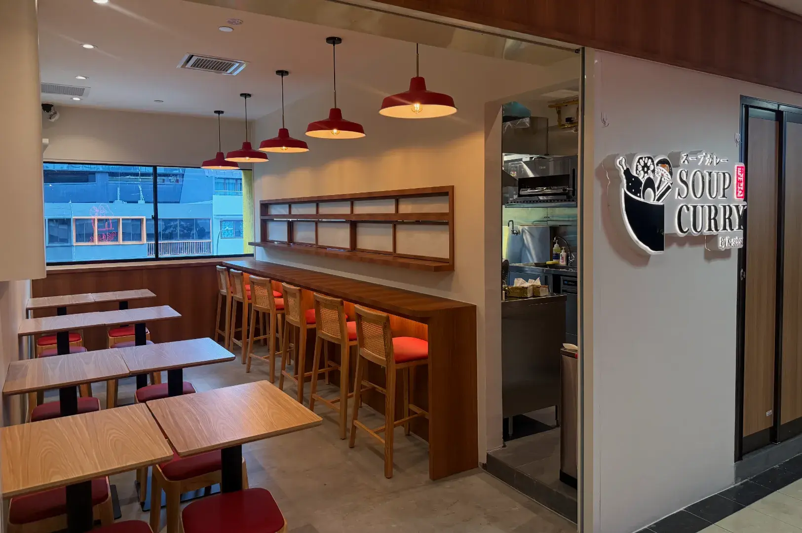 A cozy restaurant interior featuring wooden tables and high stools, with a sign for "Soup Curry" on the wall and a visible kitchen area.