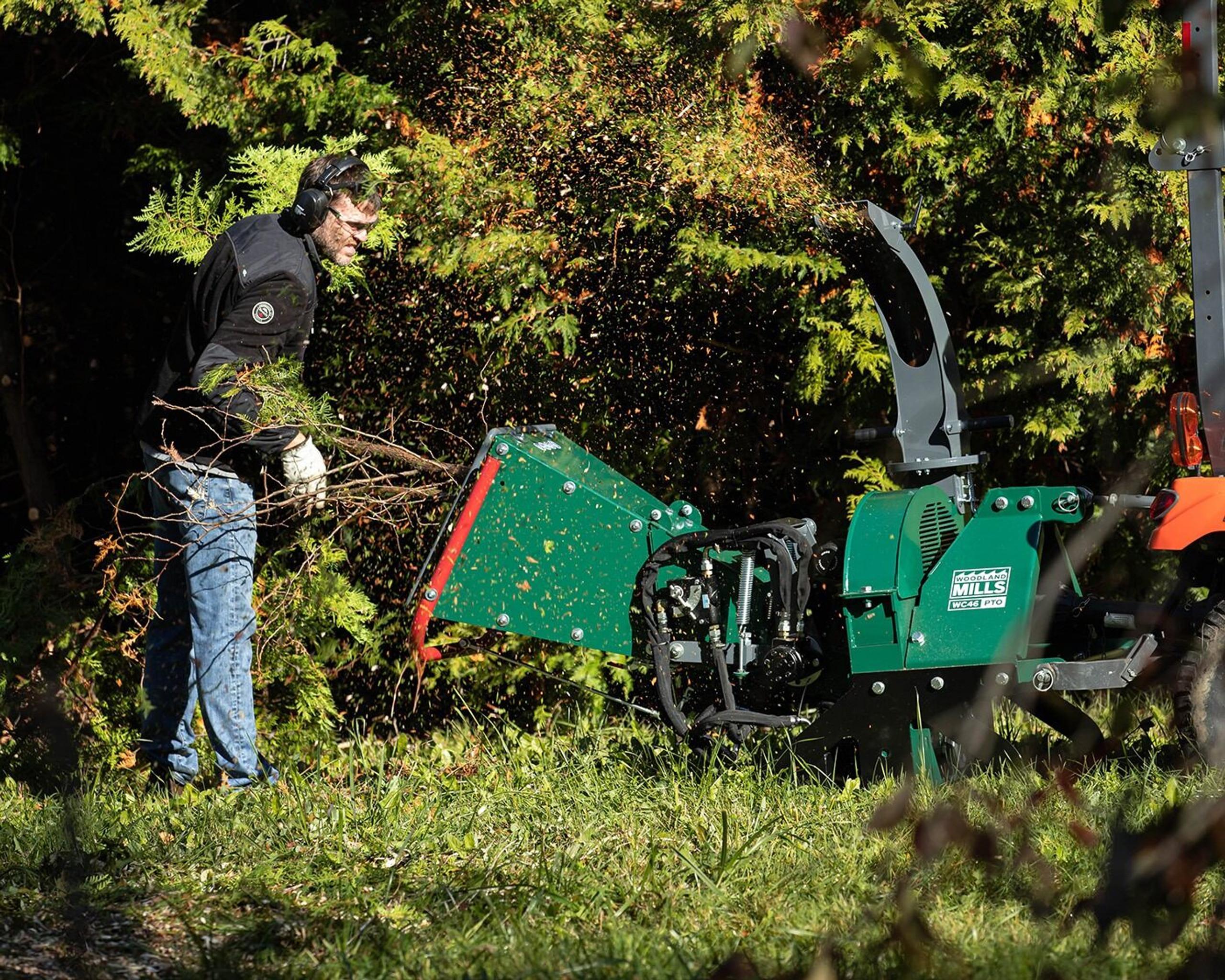 A man feeding a tree branch into a Woodland Mills WC46 Wood Chipper.