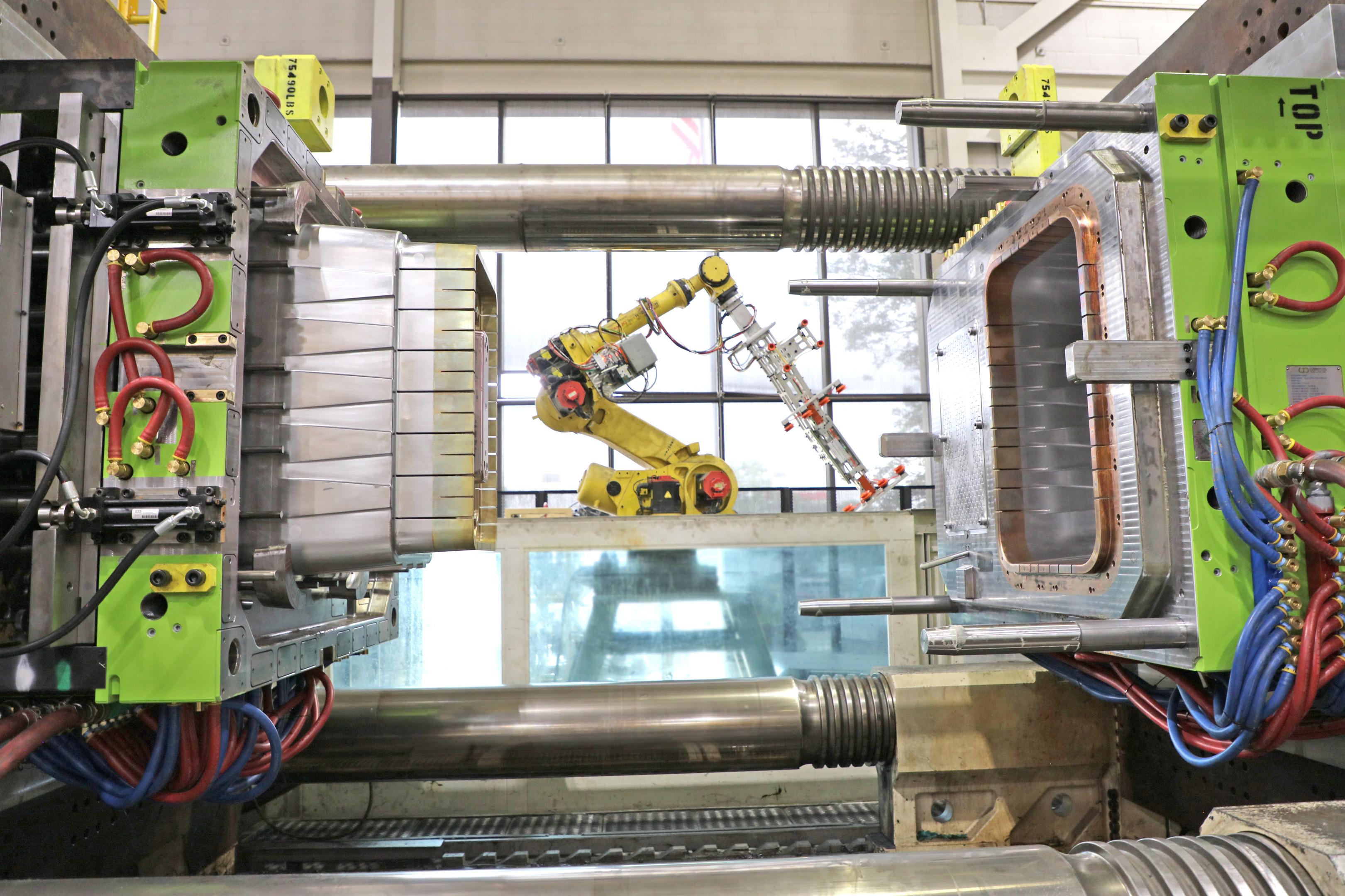 The image depicts a large industrial injection molding press with its platens open, showcasing the interior of a manufacturing facility. This setup is essential for processes like plastic injection molding, where molten plastic is shaped into various components for mass production of consumer products and medical devices.