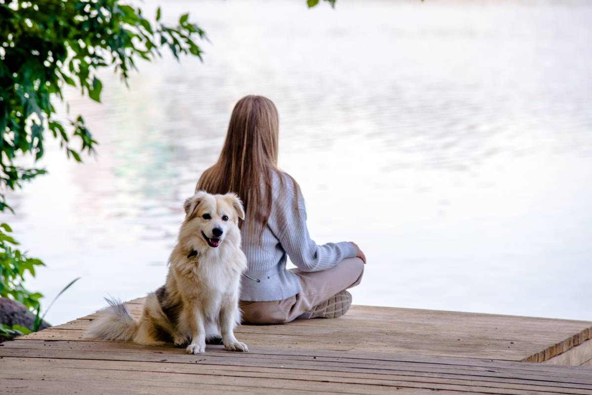 A woman meditates by a peaceful lake with her happy dog beside her, capturing the essence of Tips for Beginners in Meditation for Dogs