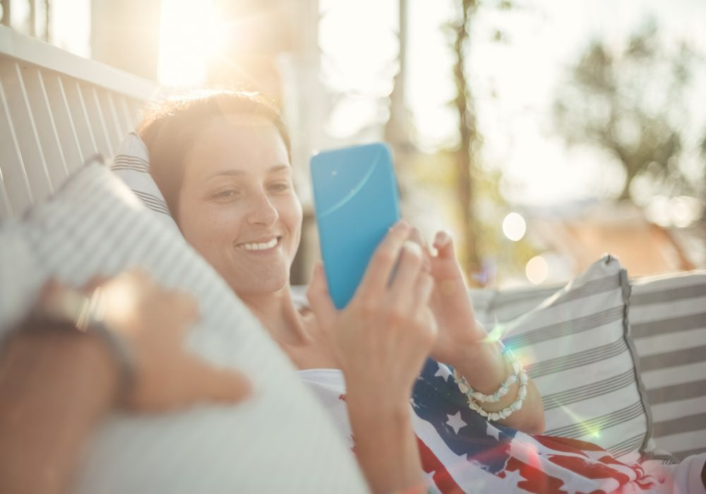 Pretty young woman sitting on a porch swing and checking her cell. 