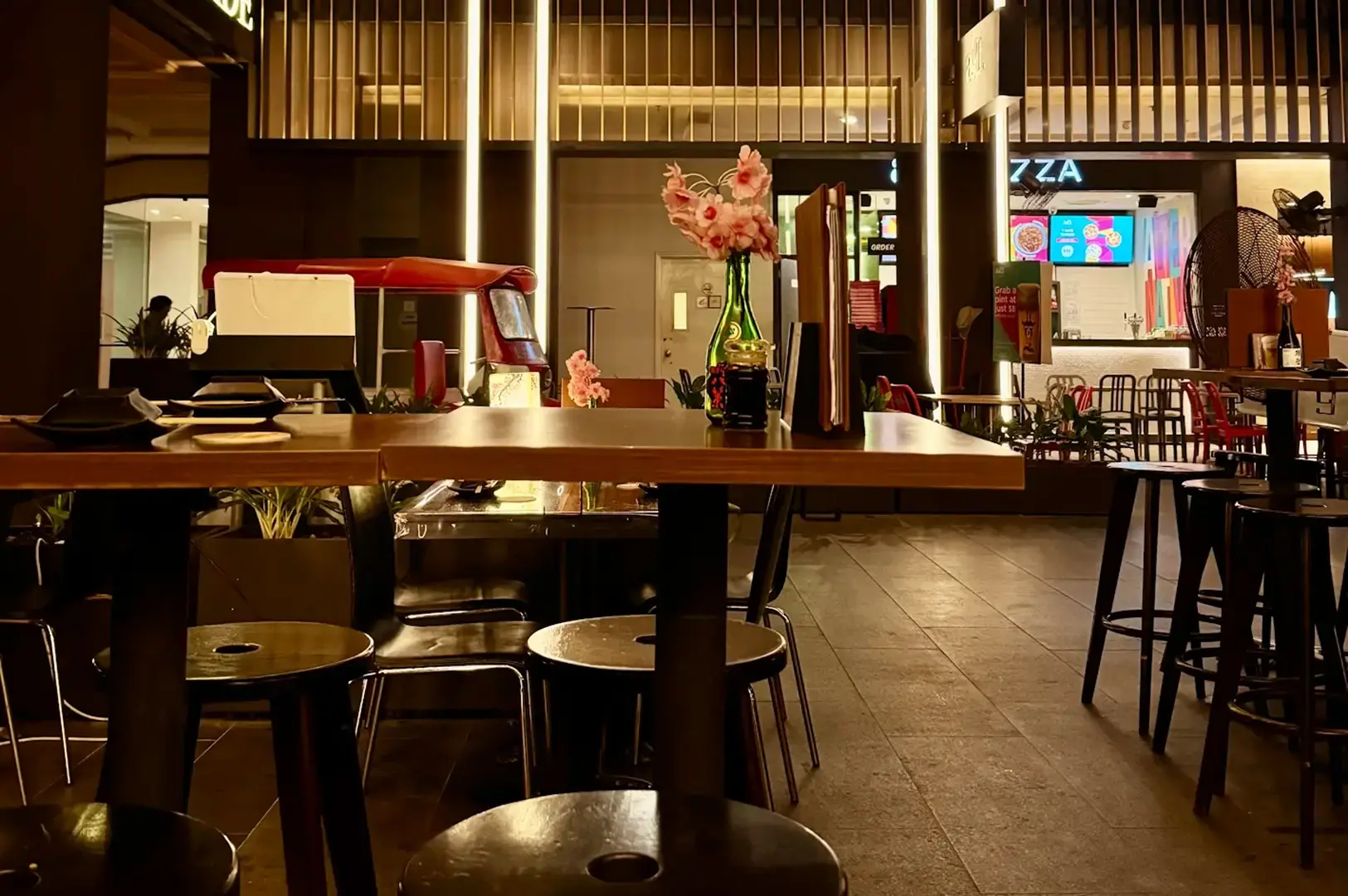 Warmly lit TEN Sushi Bar dining area with wooden tables, stools, floral decor, and a shopping-centre interior in the background.
